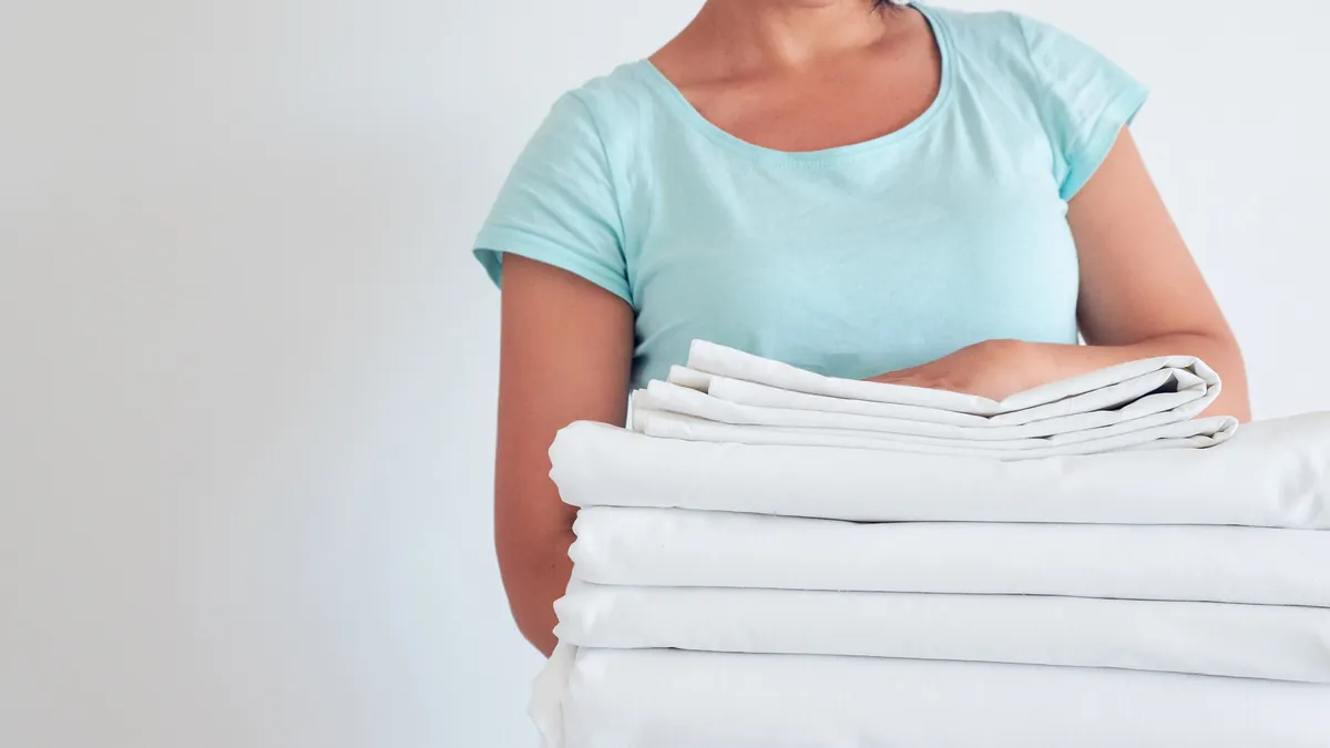 A person holding a neat stack of freshly laundered white sheets