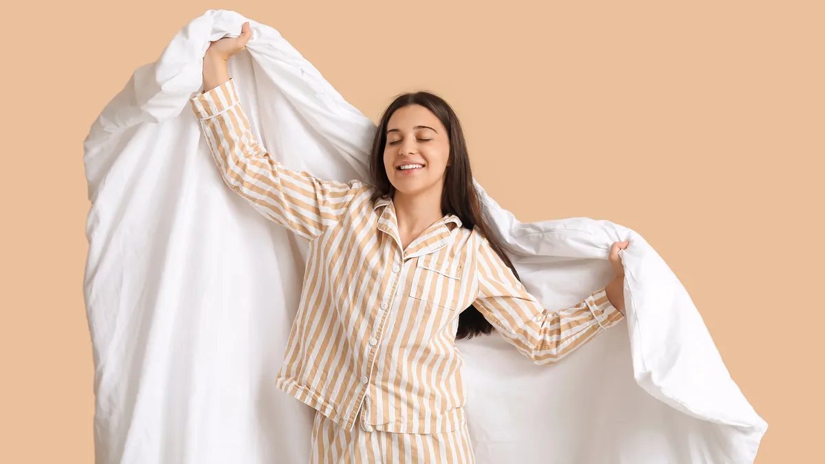 A woman in striped pyjamas holding up a freshly washed white doona